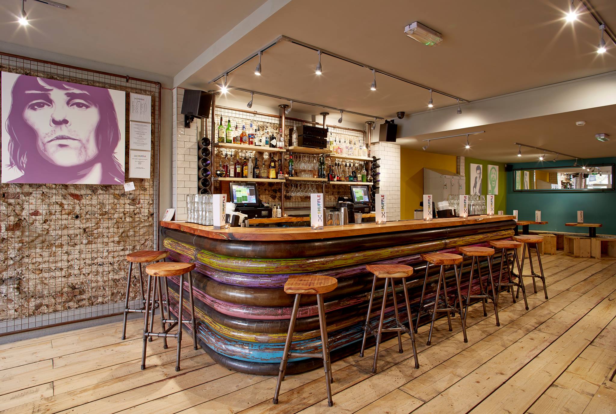 Bar stools around bar with drinks behind and a photo in a frame hanging down.