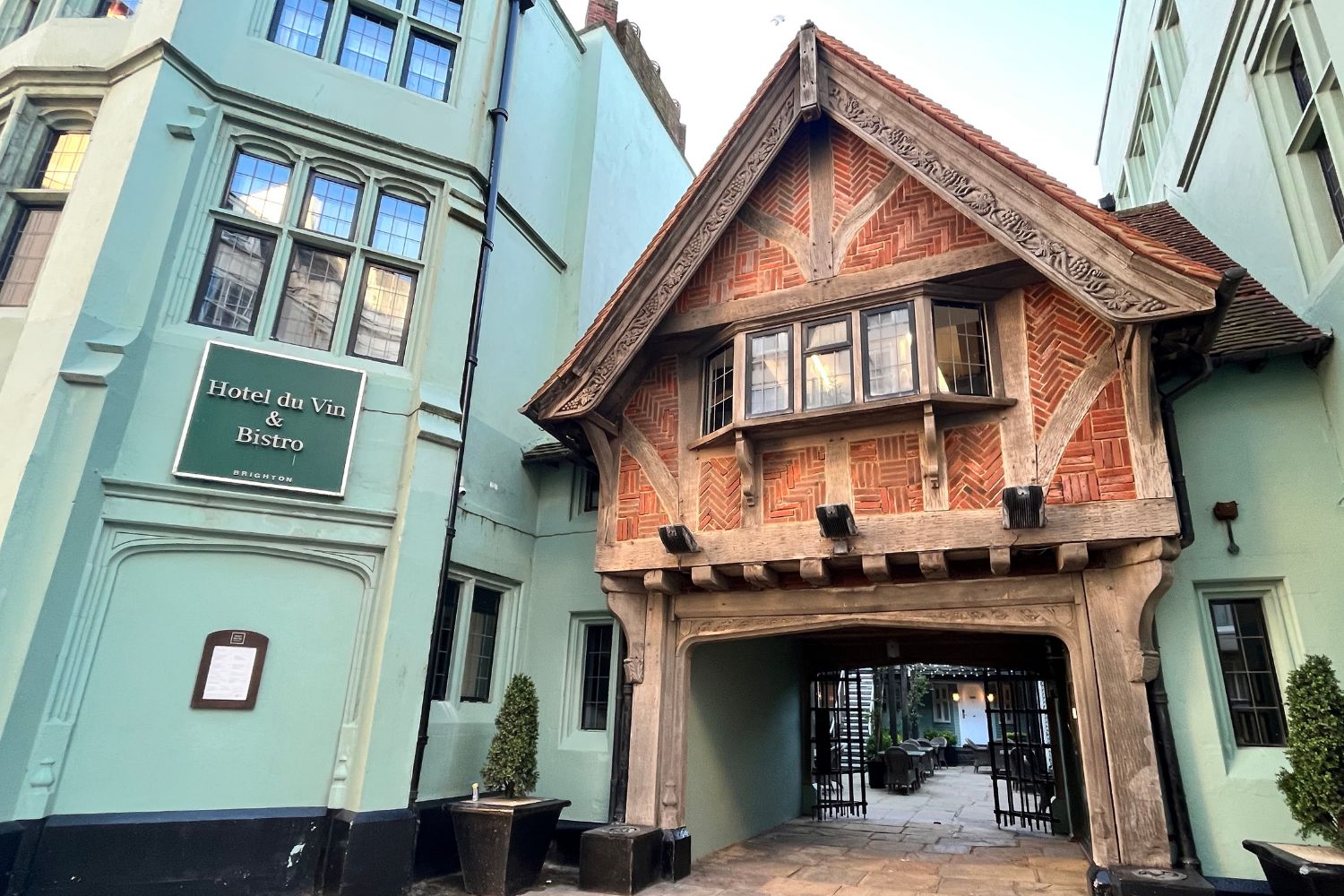 Outside of hotel featuring a green building with a dark green sign that says Hotel Du Vin and a wooden building in the middle