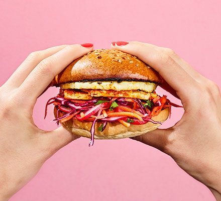 Pink background with a persons hands holding a burger