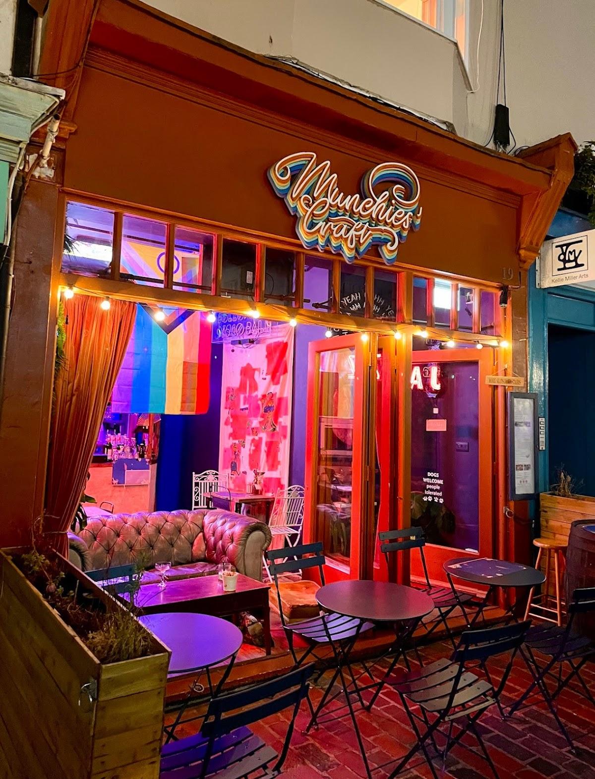 Outside view of a cafe with seats outside, neon lights and a pride flag