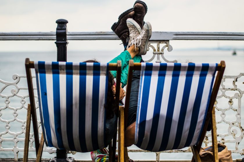 People sitting on white and blue striped beach chairs with only their shoes showing in the air