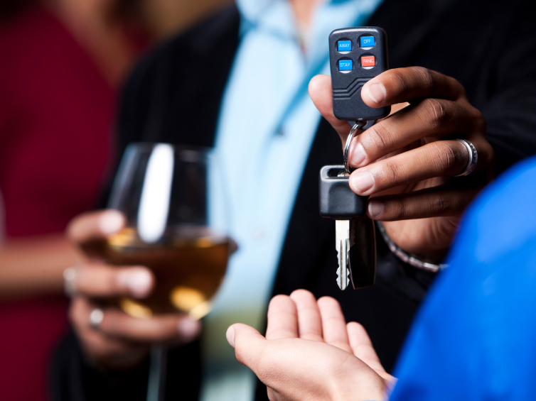 Man in a suit holding a wine glass handing car keys to a man in a blue shirt