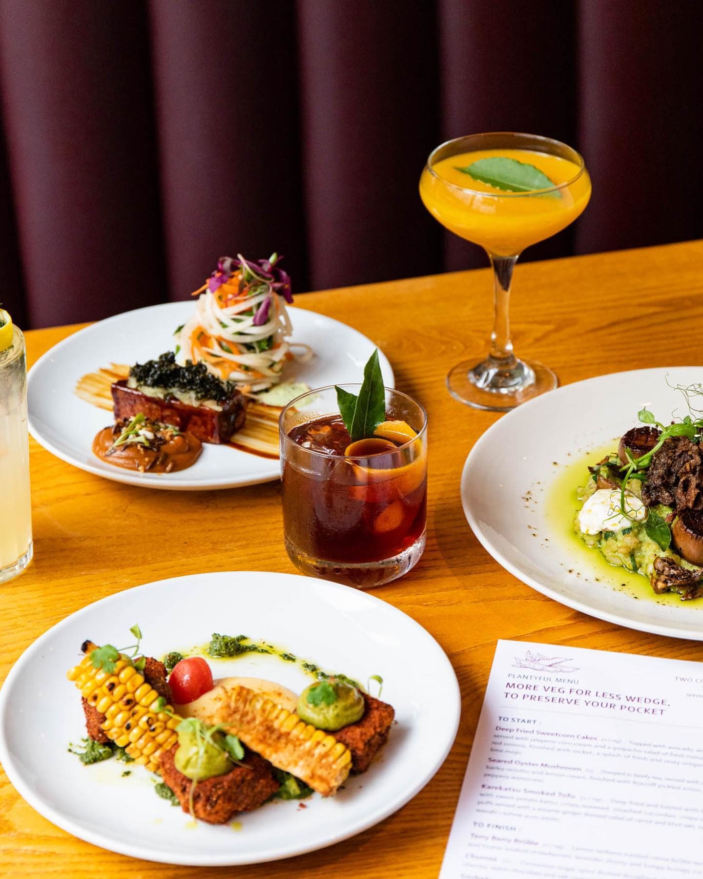 A table with plates showing vegetarian and vegan dishes alongside glasses with cocktails and cold drinks.