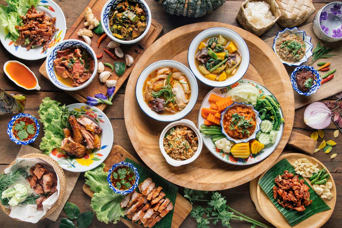 Image of a table with wooden plates filled with different Thai cuisines.