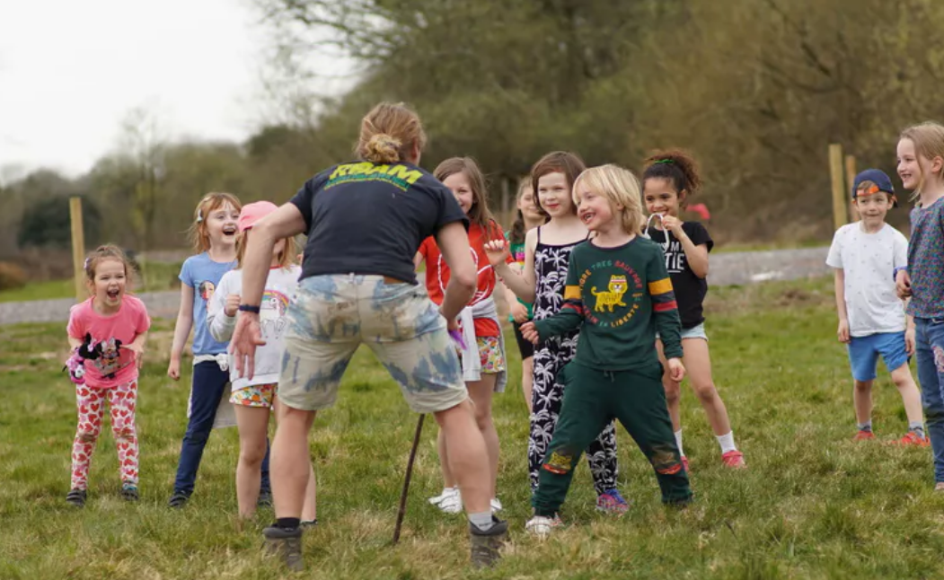 group of children outside with a man telling them instructions on the outdoor activity they are involved in