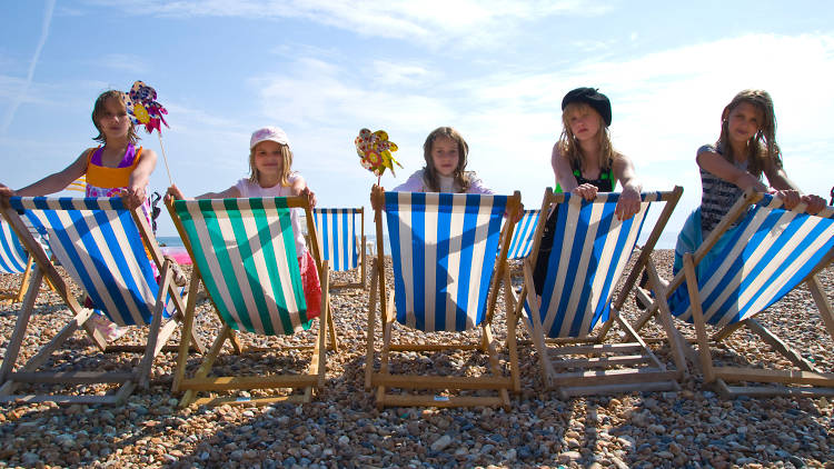Group of children on the beach sitting on blue and white striped beach chairs