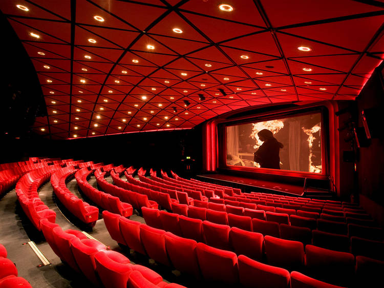 A room with a red ceiling with lights, red chairs and a movie screen.