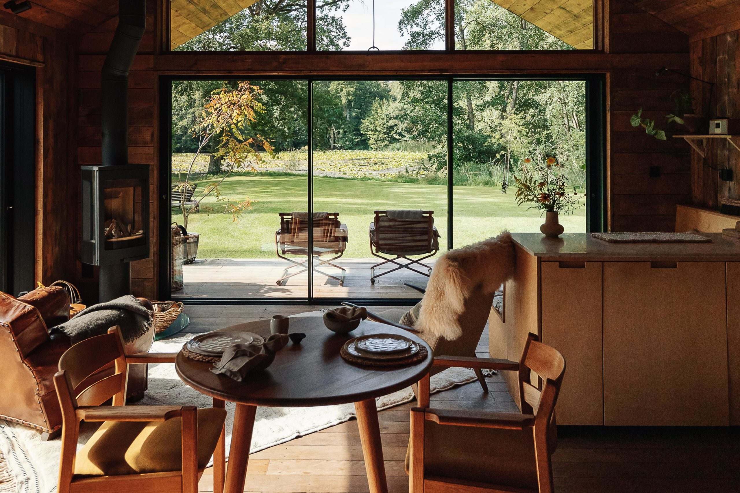 two wooden chairs positioned on either side of a wooden table, in front of a white sofa and windows which show the view of a garden.