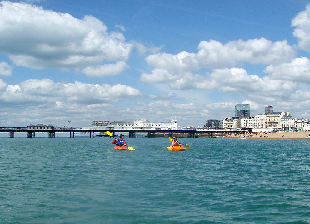 two people in kayaks in the middle of the sea and with a pier behind them