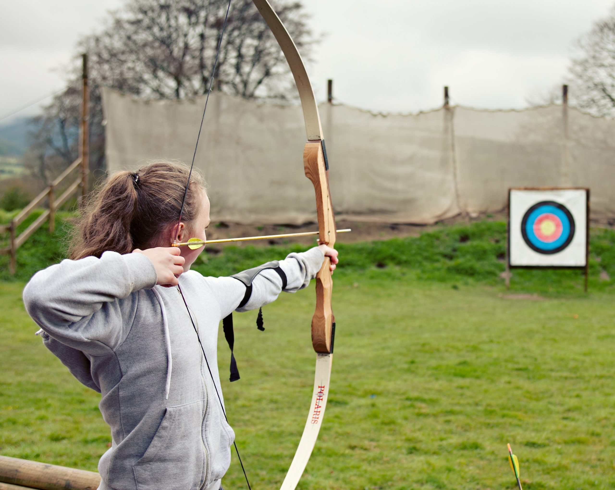girl aiming bow and arrow at blue, red and yellow target