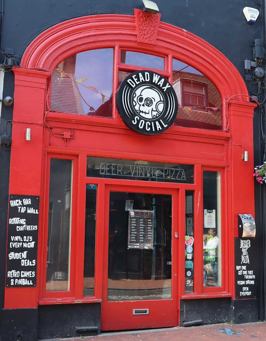 Red arched door which has a logo with a skeleton that says "Dead Wax Social"