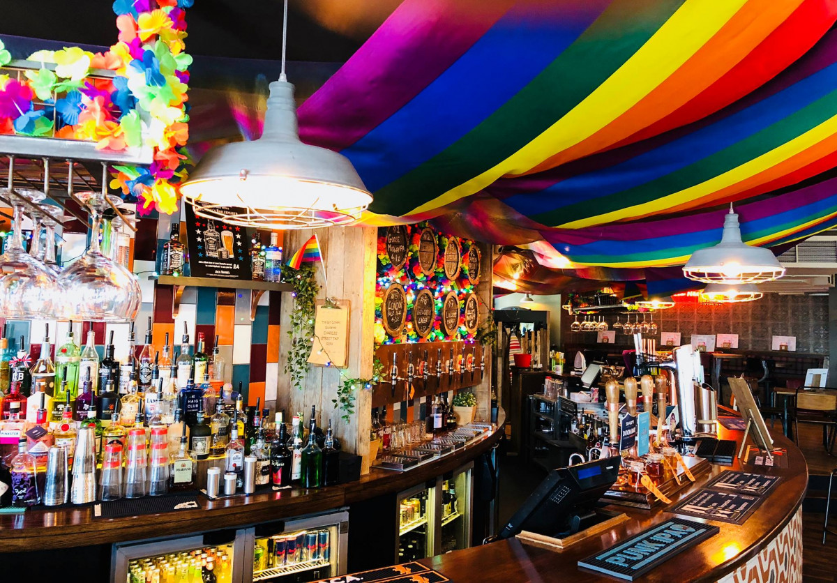bar with lots of drinks and rainbow flags and necklaces