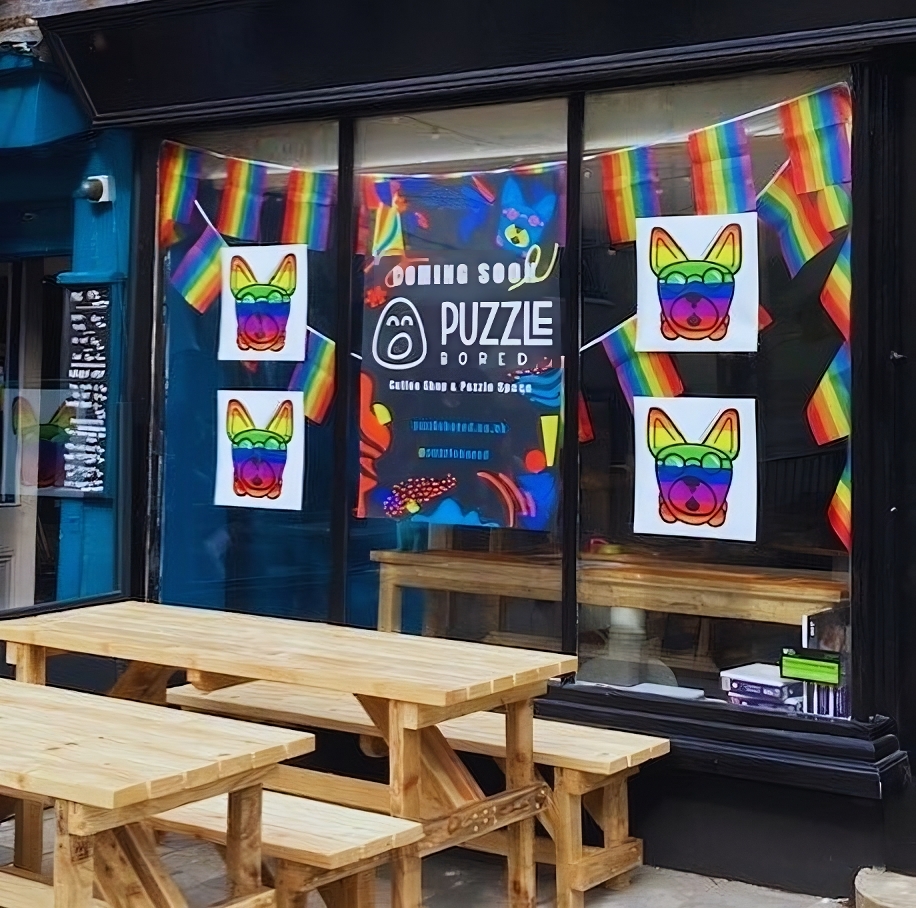 Wooden benches outside the puzzle bored café which has rainbow flyers and rainbows in the windows.