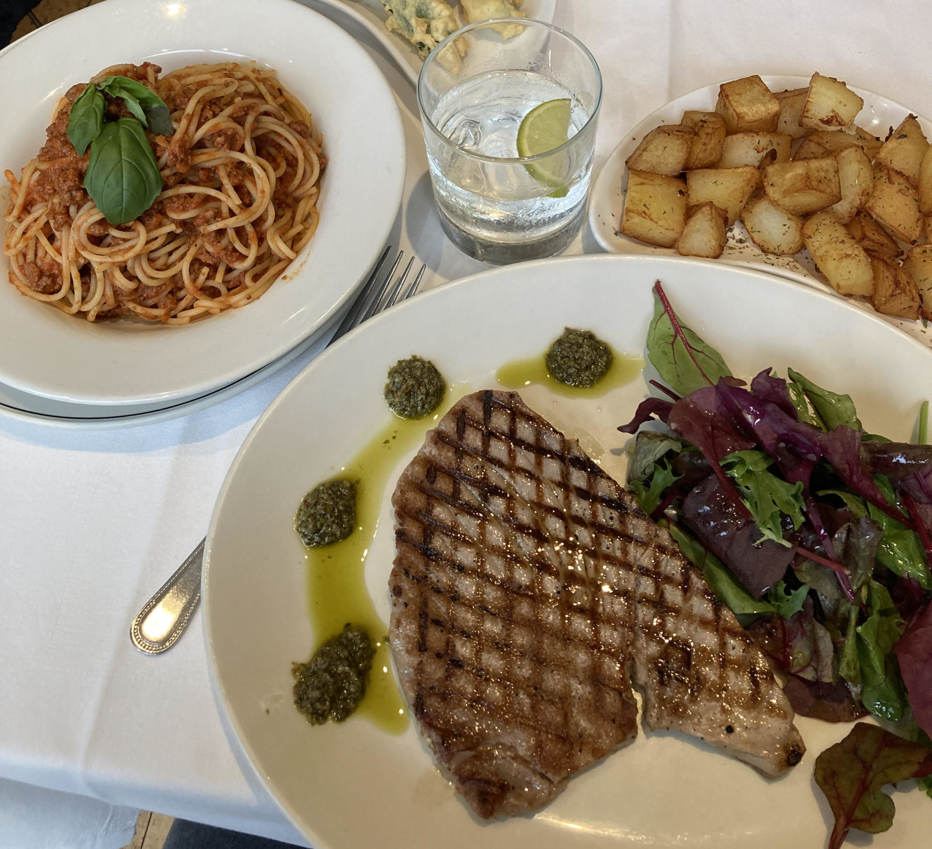 A table set with plates offering spaghetti in tomato sauce, potatoes and a steak with a salad.