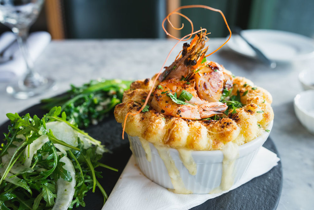 lobster with potatoes in a bowl with some green vegetables on a plate