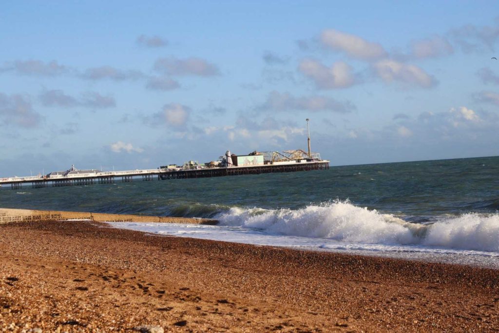 Sand and waves with Brighton Pier in background.