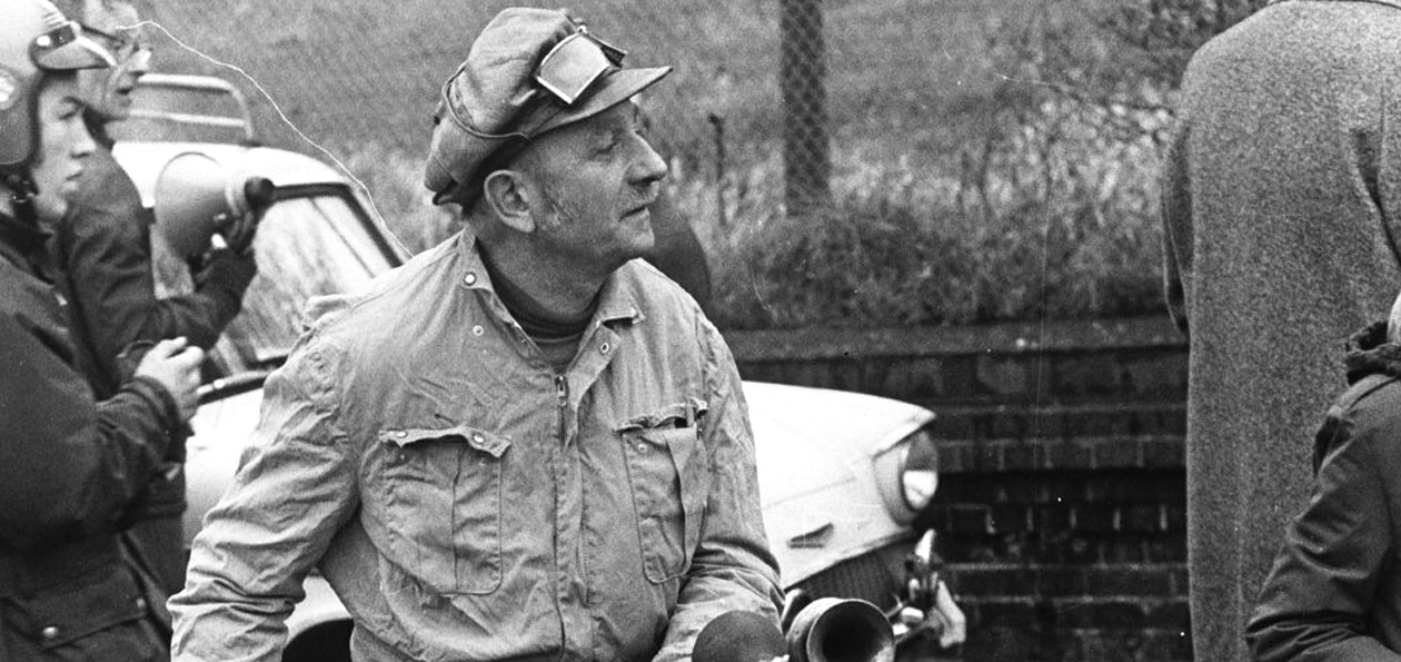 Black and white photo of a man standing in front of car