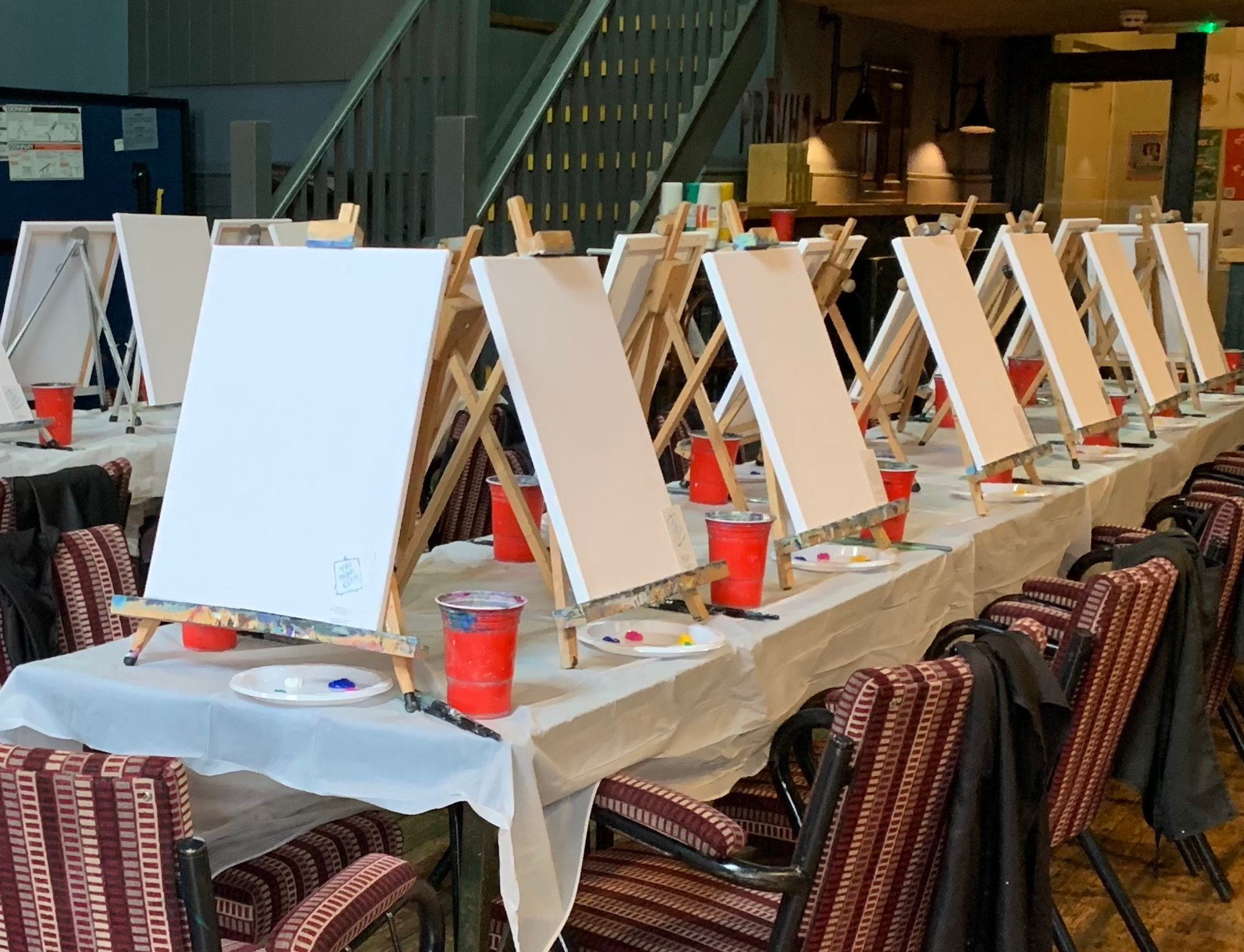 An array of blank canvases set up on table with chairs