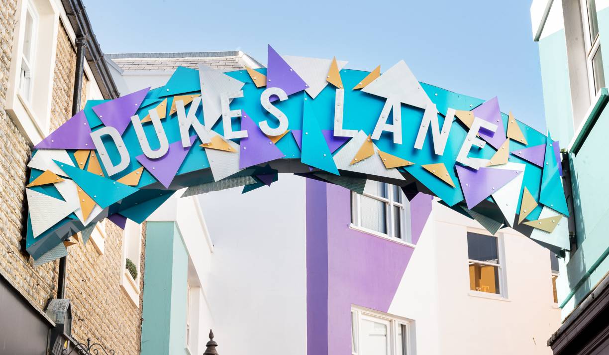 A colourful blue, purple, white and yellow sign which says Dukes Lane