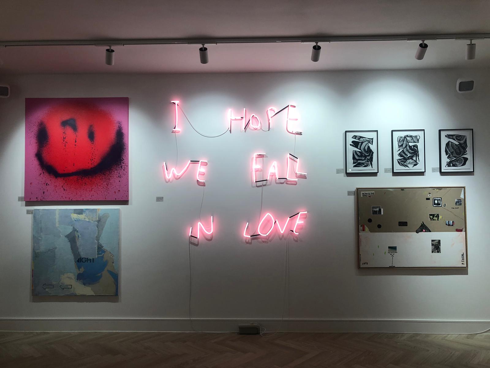 Art on wall including a neon sign which says I hope we fall in love at Helm Art Gallery in Brighton