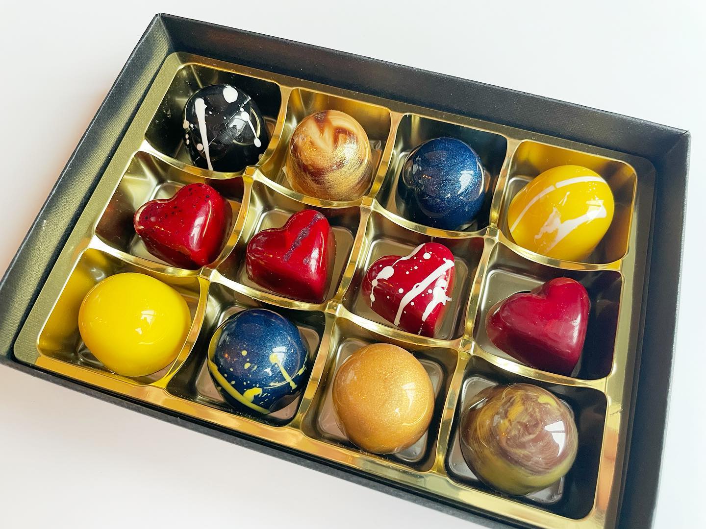 blue, yellow, red, black chocolates in box on white table made by Brighton Cacao Company chocolate shop in Brighton