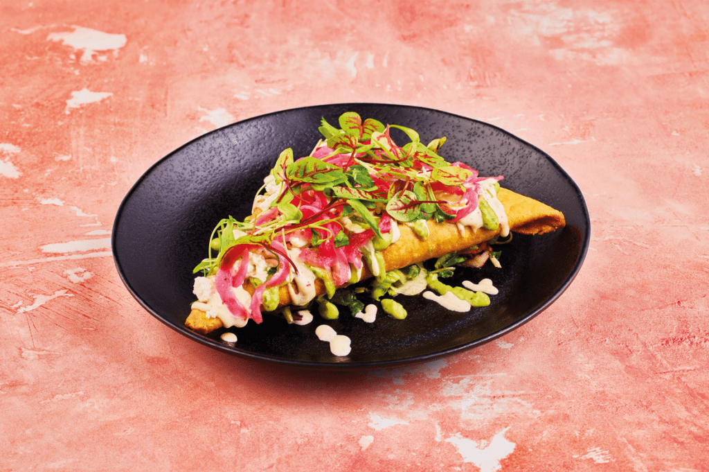 Seasonal Vegetable Tetela on a black plate and pinkish background served at wahaca in brighton as part of veganuary